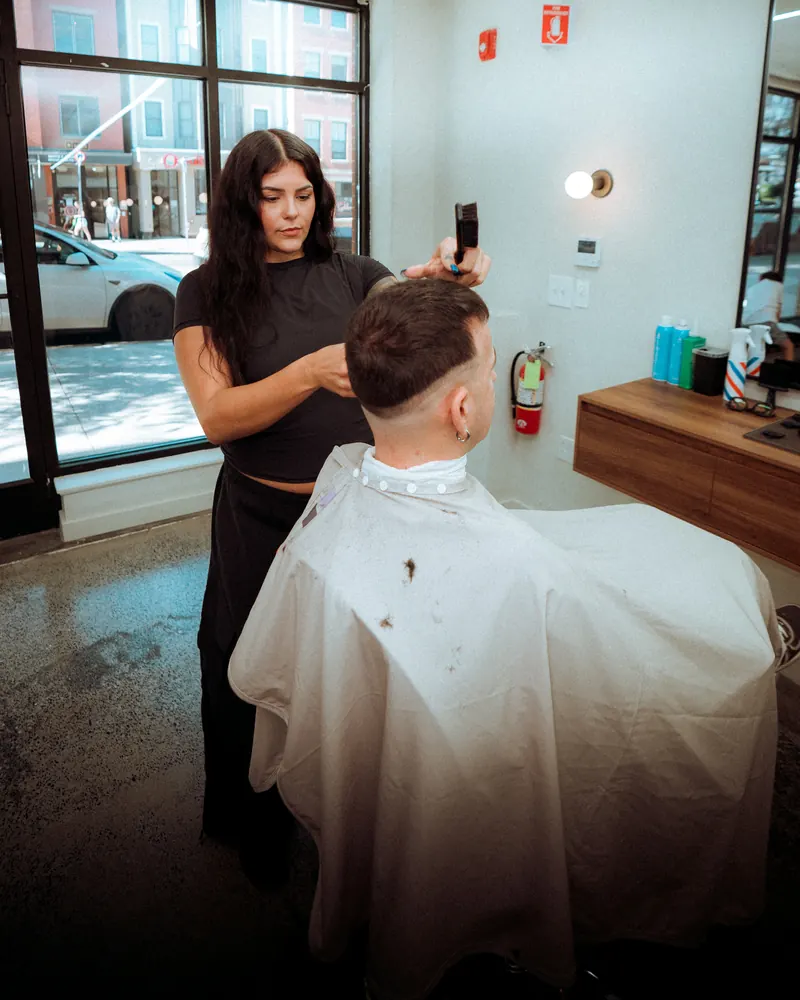 Ciera finishing a fade by the front window, clipper in hand